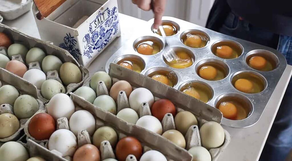 hand scrambling egg in a muffin tin with more eggs surrounding the muffin tin