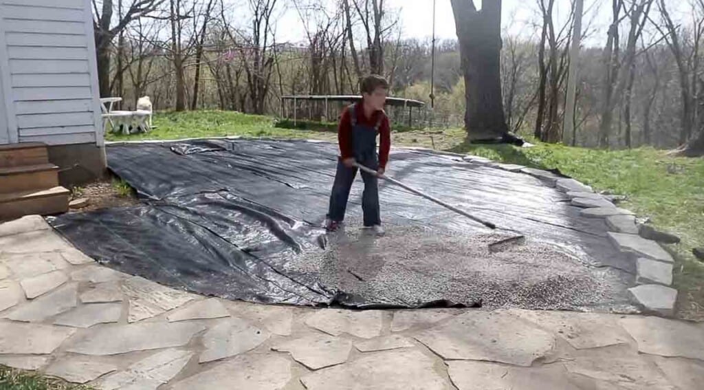 boy raking pea gravel over black plastic 