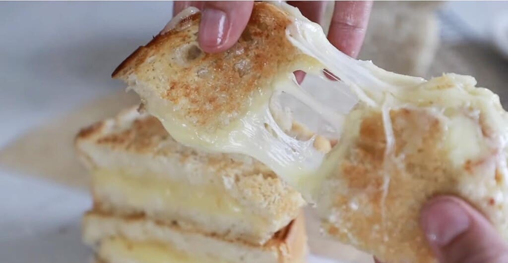 hands pulling apart grilled cheese with gooey cheese strung between the pieces