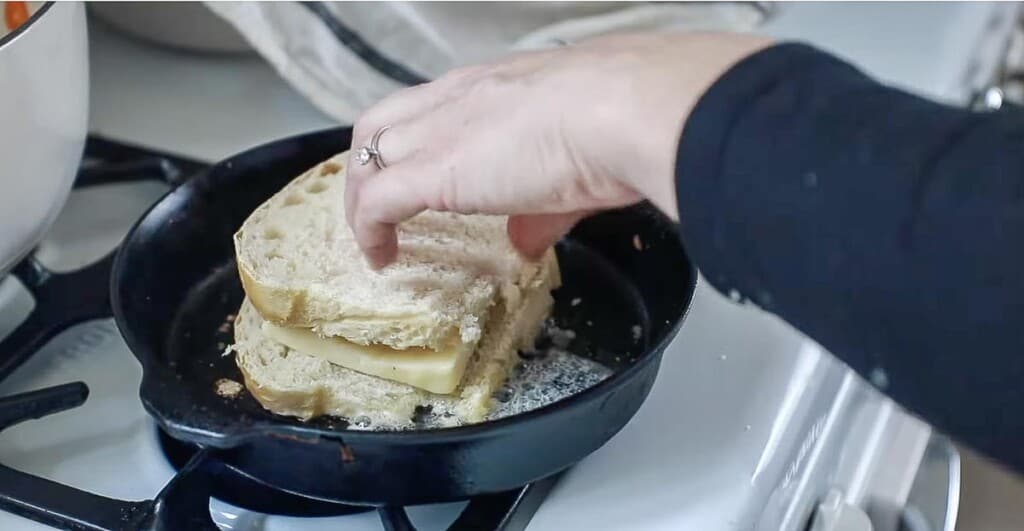 hand adding a slice sourdough bread on top of another piece of bread topped with cheese