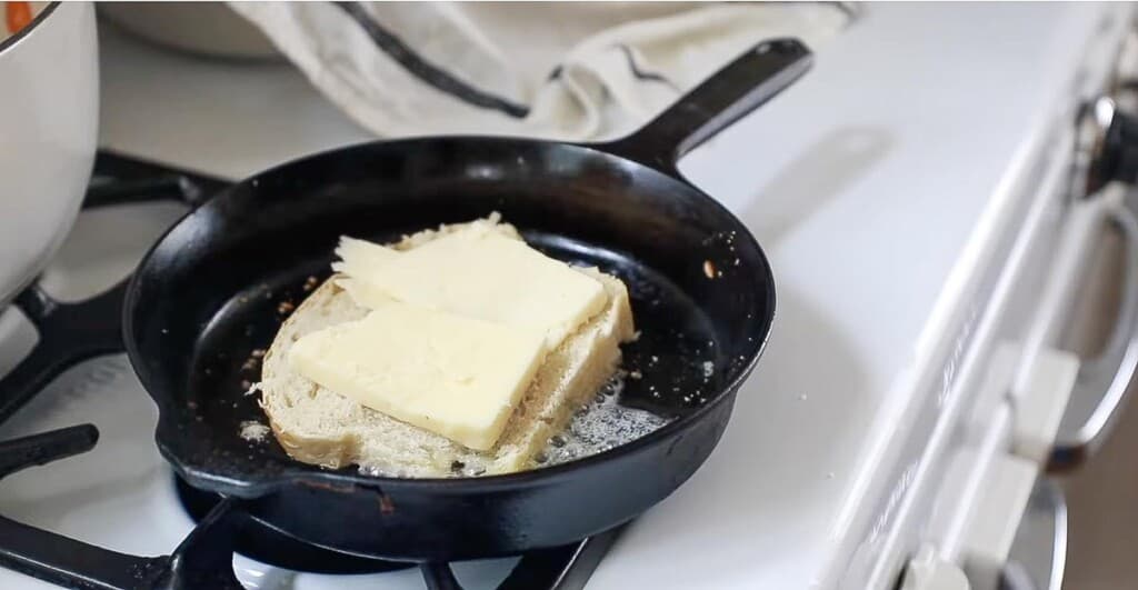 sourdough bread topped with sliced cheese on a cast iron skillet on a white vintage stove.
