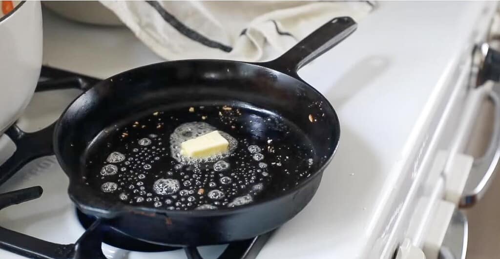 butter melting on a cast iron skillet on a white vintage stove