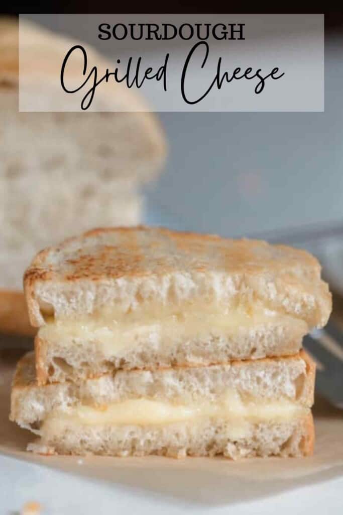 sourdough grilled cheese stacked on top of each other on parchment paper with a loaf of sourdough sandwich bread in the background