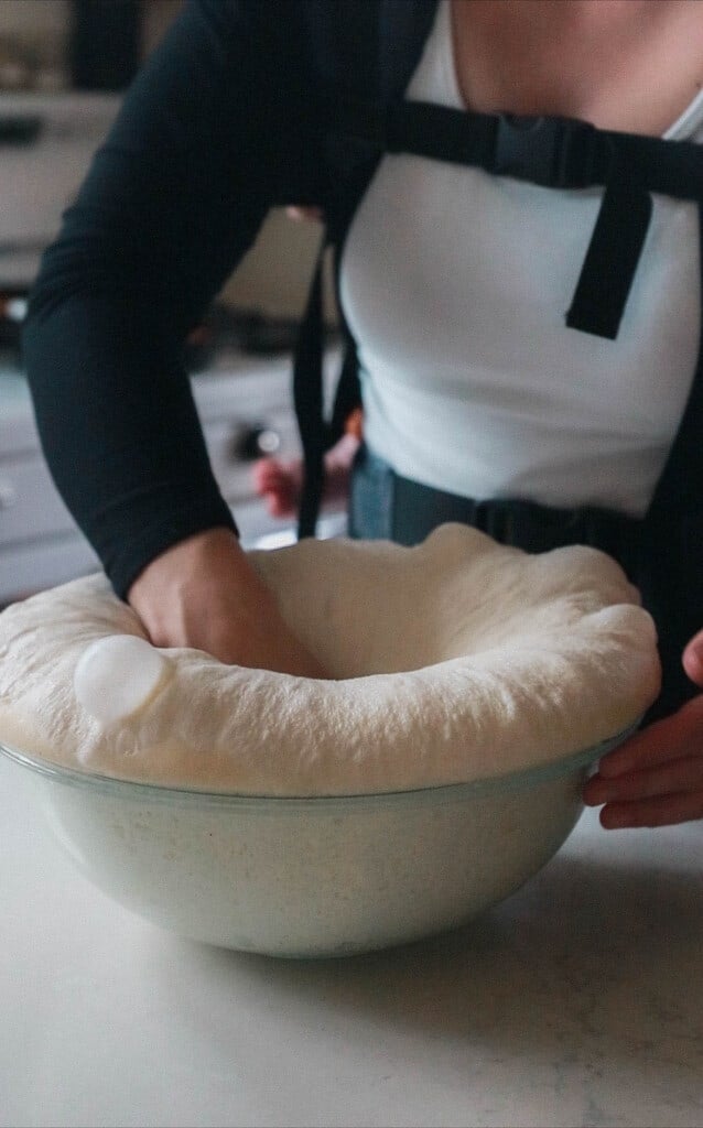woman punching down sourdough bread dough in a glass bowl