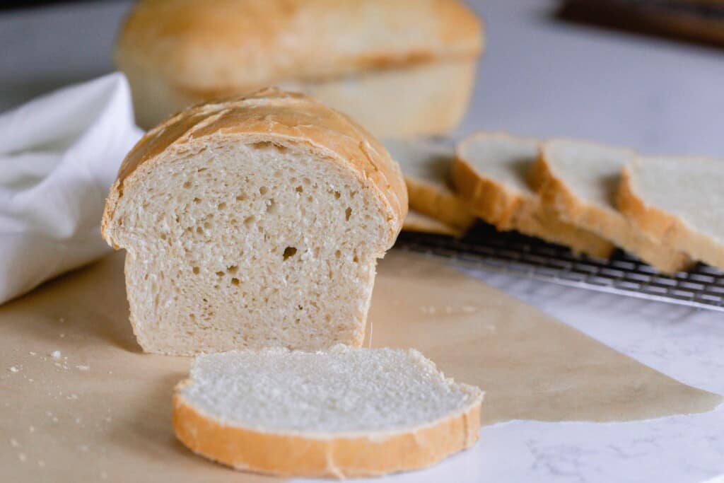 loaf of sourdough sandwich bread on parchment paper with a slice sliced off the loaf