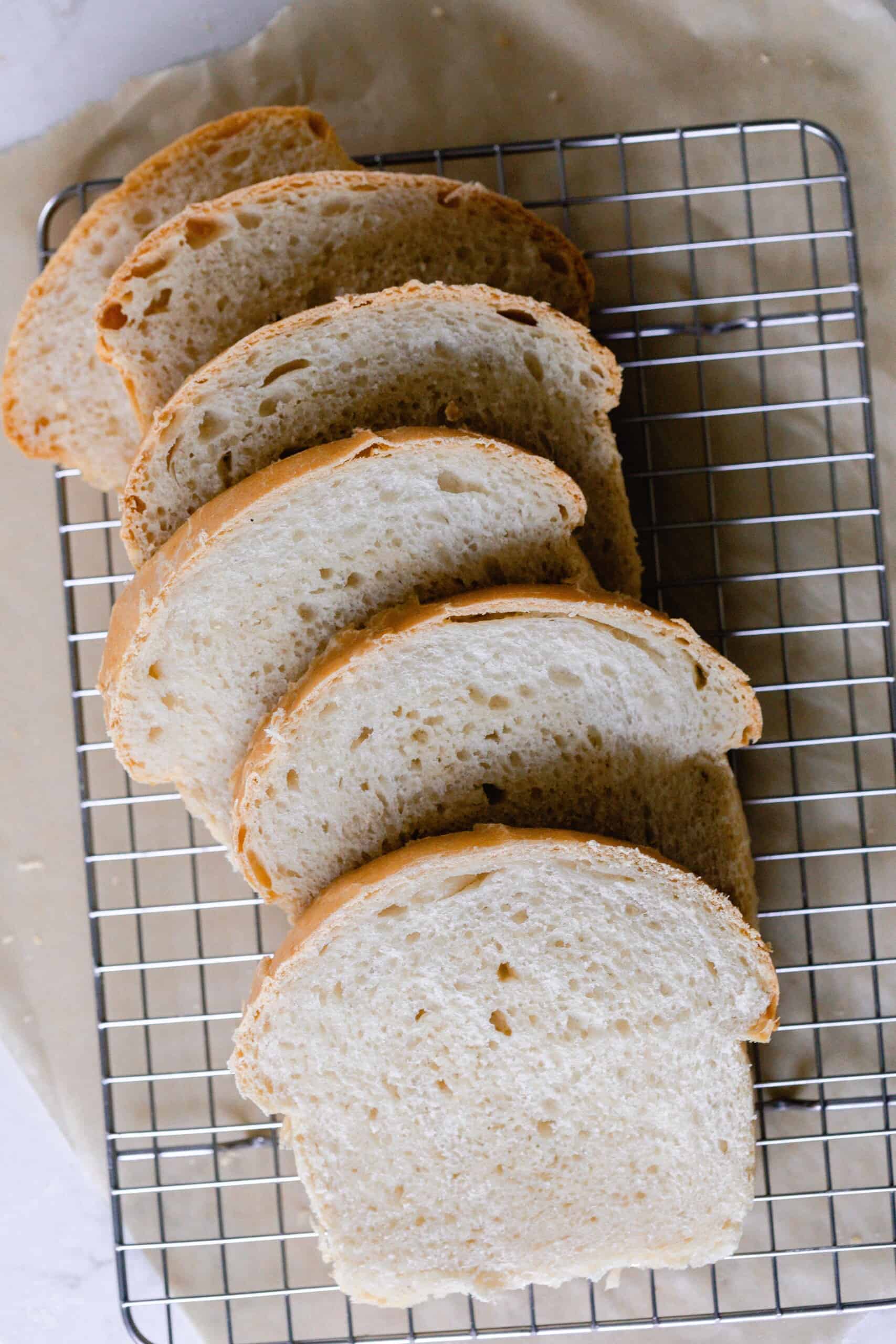 six slices of sourdough sandwich bread spread out on a wire rack over parchment paper