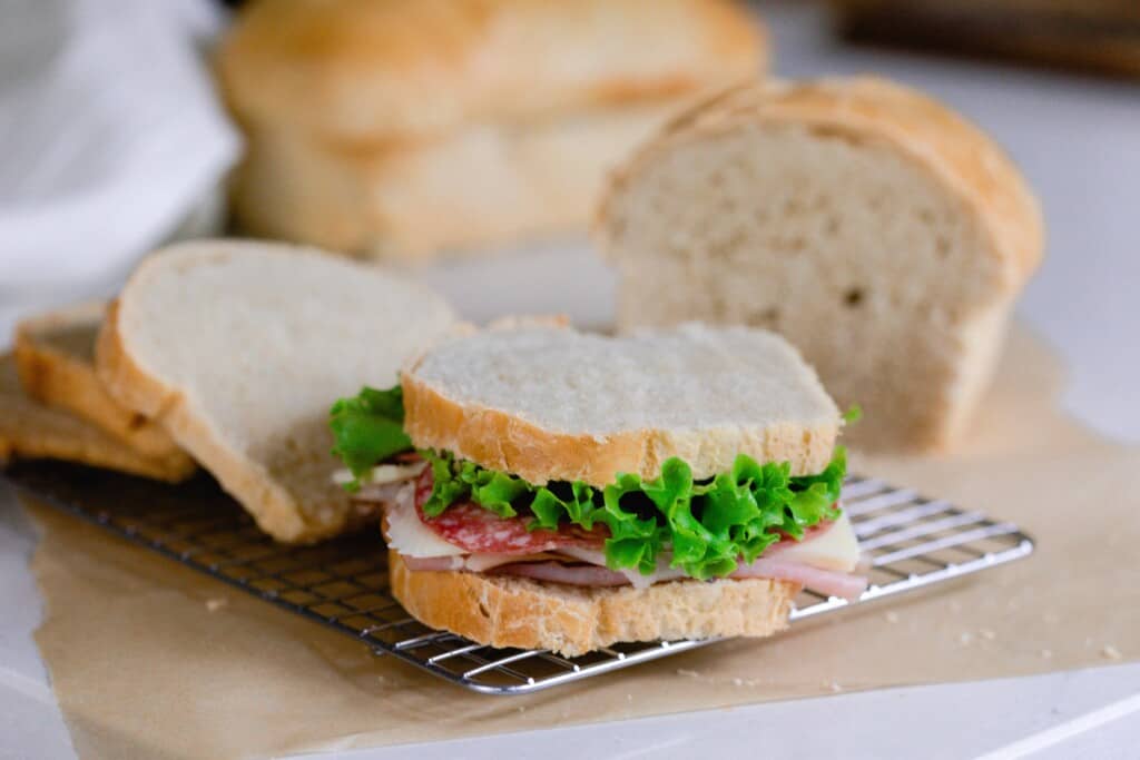 sandwich made with lettuce, tomato, turkey on freshly sliced sourdough bread on a wire rack with more bread in the background