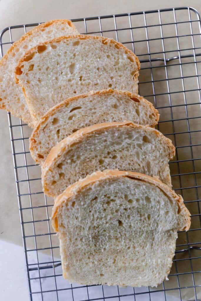 four slices of sourdough sandwich bread spread out on a wire cooling rack over parchment paper