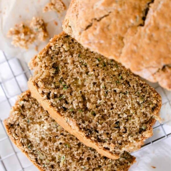 A loaf of zucchini bread with two slices cut and laying on a wire rack.