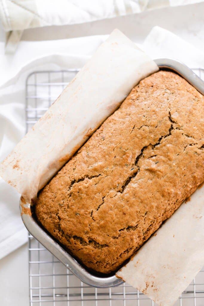 overhead photo of sourdough zucchini bread in a parchment lined stainless steel loaf pan on a wire rack over a white towel