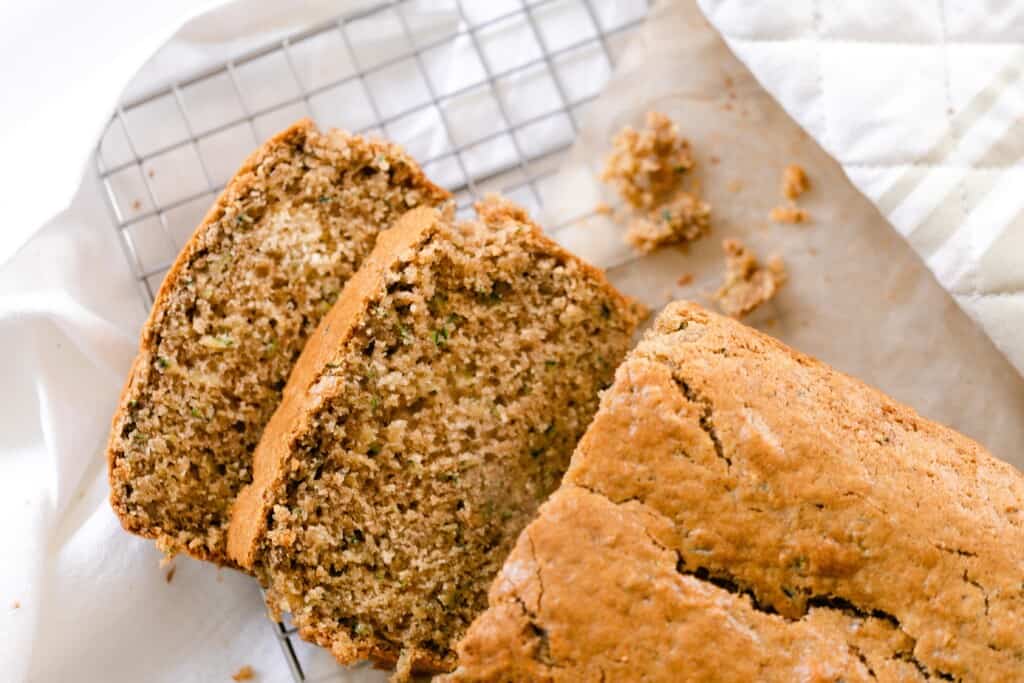 loaf of sourdough zucchini bread with two slices laying down on a wire rack