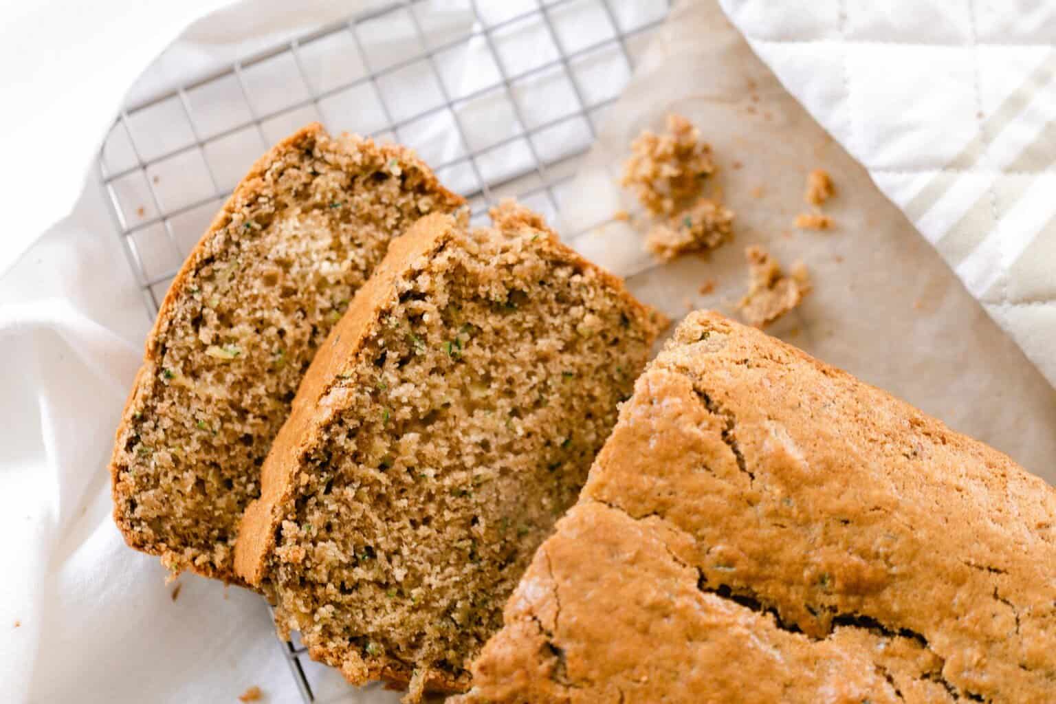 loaf of sourdough zucchini bread with two slices laying down on a wire rack