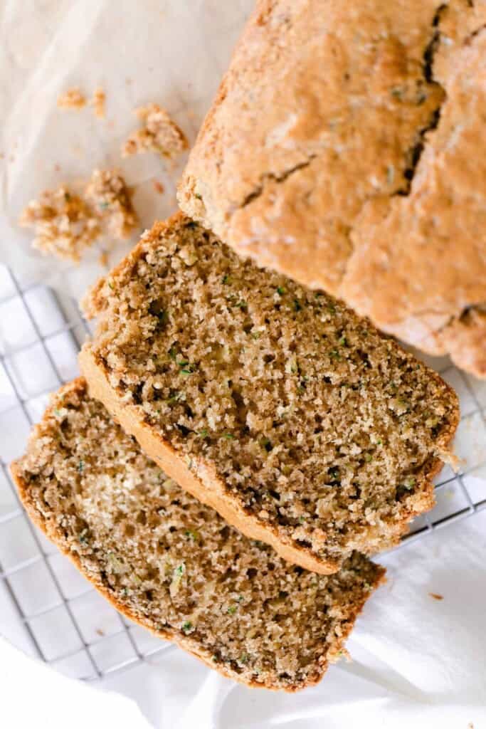 a loaf of sourdough zucchini bread with two slices layer out in from to the loaf on a wire rack