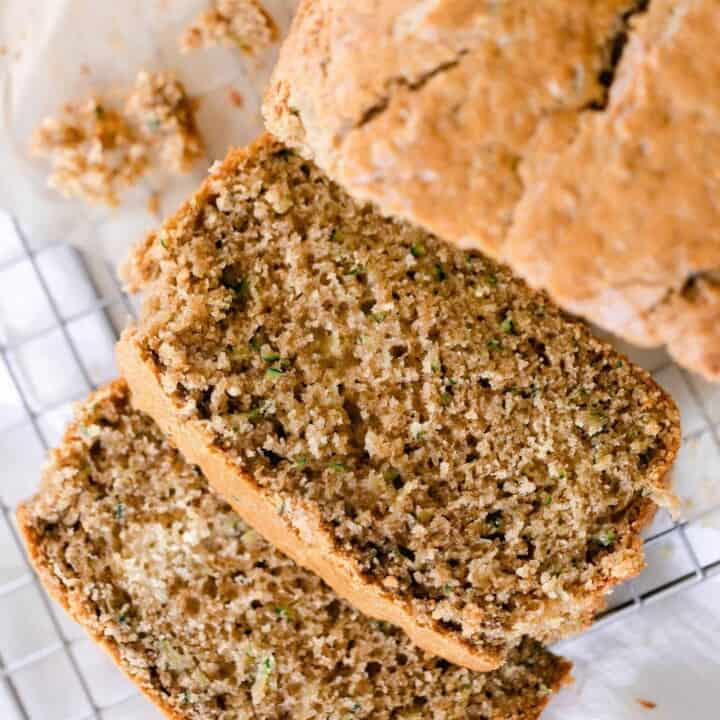 a loaf of sourdough zucchini bread with two slices layer out in from to the loaf on a wire rack