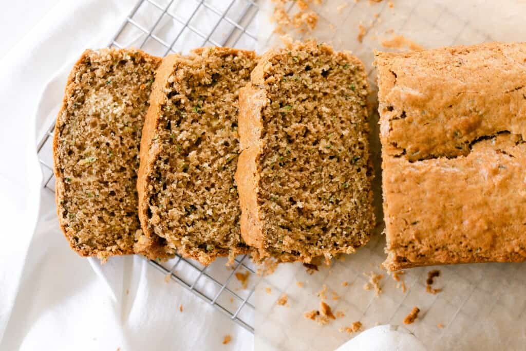 A loaf of sourdough zucchini bread with the slices of bread to the left on a wire rack over a white towel