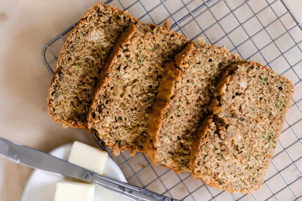 four slices of sourdough zucchini bread on a wire rack with a little white plate with butter and a knife in front