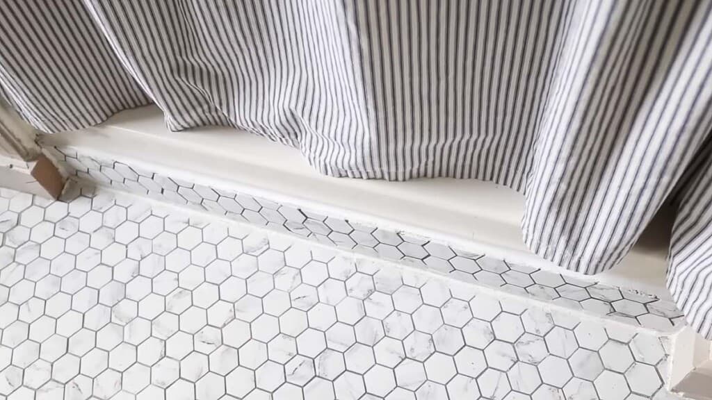 marble hexagon floor next to a shower with a ticking stripe shower curtain