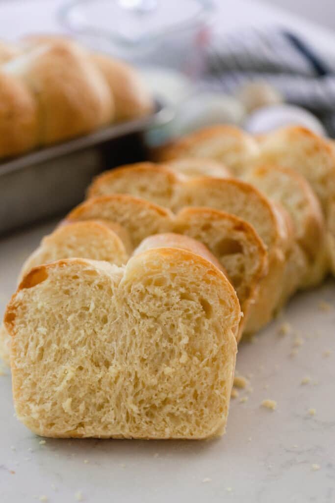 thick slices of brioche bread on a white quartz countertop with another loaf of bread in a bread pan in the background