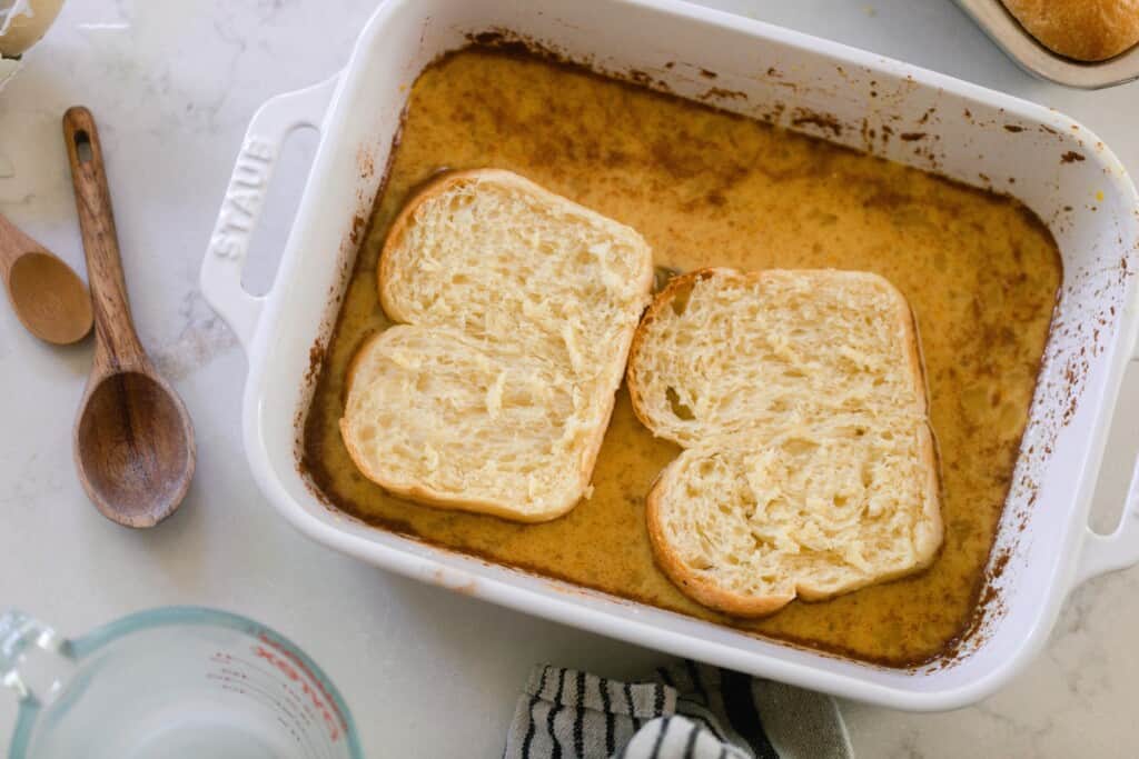 slices of brioche bread sitting in a custard mixture in a baking dish.