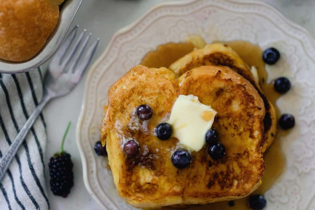 close up overhead photo of brioche French toast on a white plate with fresh blueberries