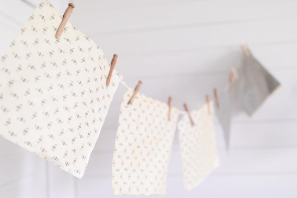 five beeswraps hanging with clothes pins on twine that is hung on a corner of a wall