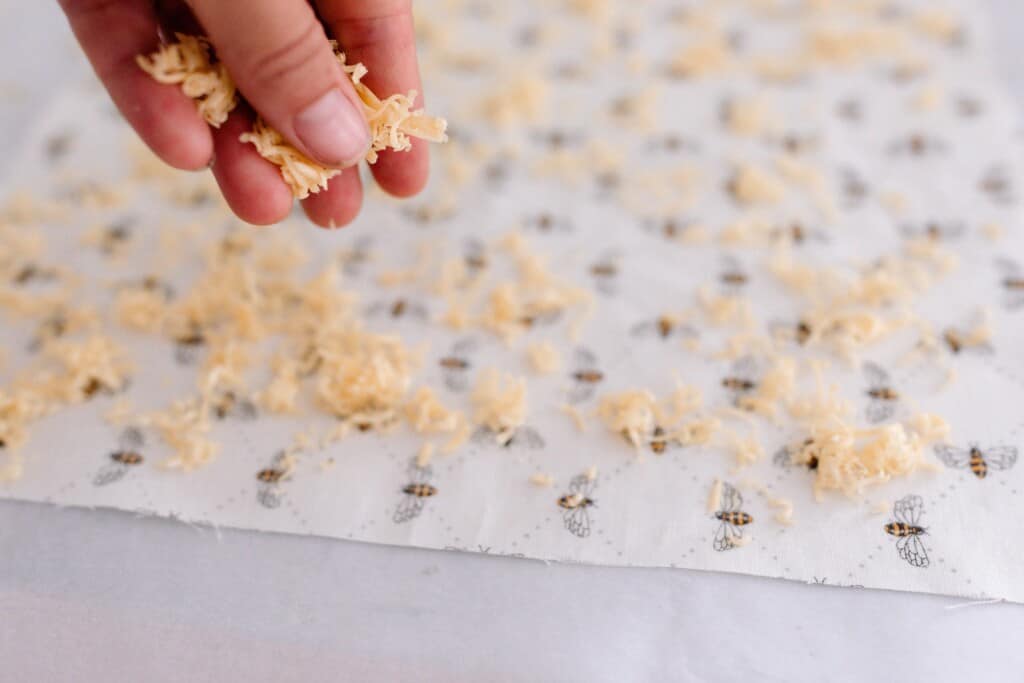 hand sprinkling grated beeswax over fabric with a bee print