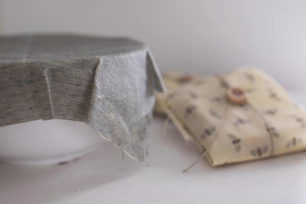 beeswax wraps formed over a white bowl and another food item wrapped in a bees wrap with a button