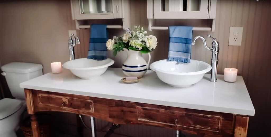 vintage inspired vanity that looks like an old desk with a marble top, vintage bowls for sinks, and medicine cabinets hanging above the vanity