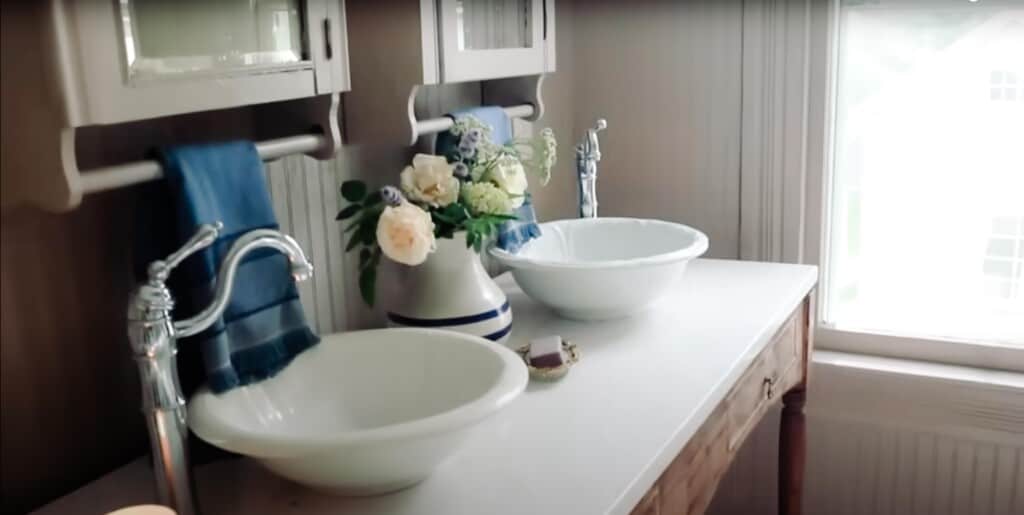 antique inspired vanity with marble top, vintage bowls for sinks, and antique looking faucets. Two antique medicine cabinets hang above the sinks