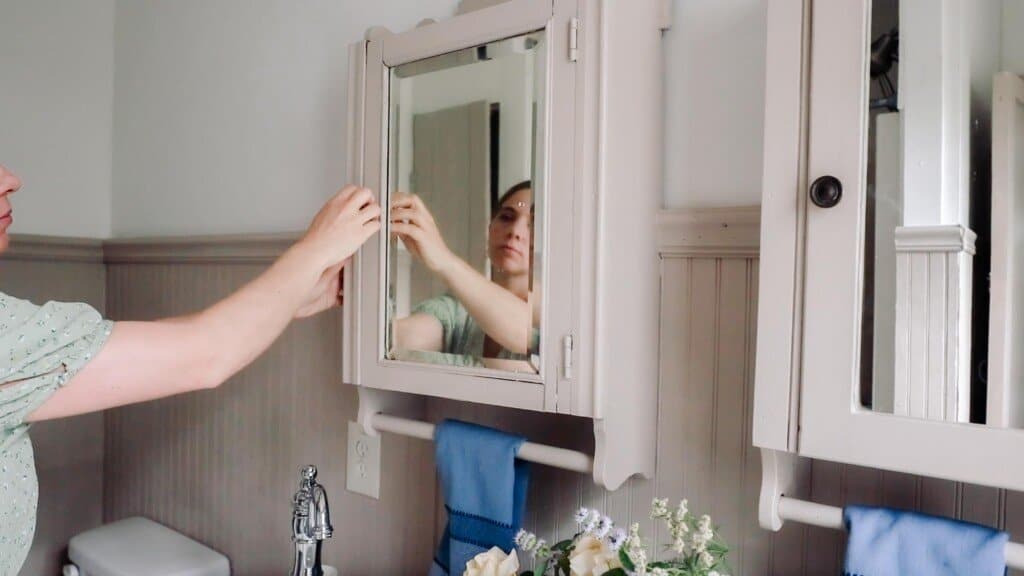 woman closing a antique medicine cabinet painted beige in a bathroom