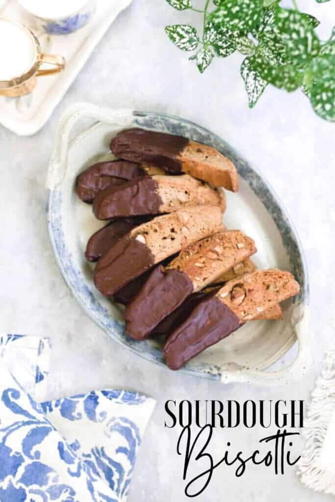 sourdough biscotti dipped in chocolate on a white and blue vintage platter on a gray countertop with a blue floral towel in the right corner