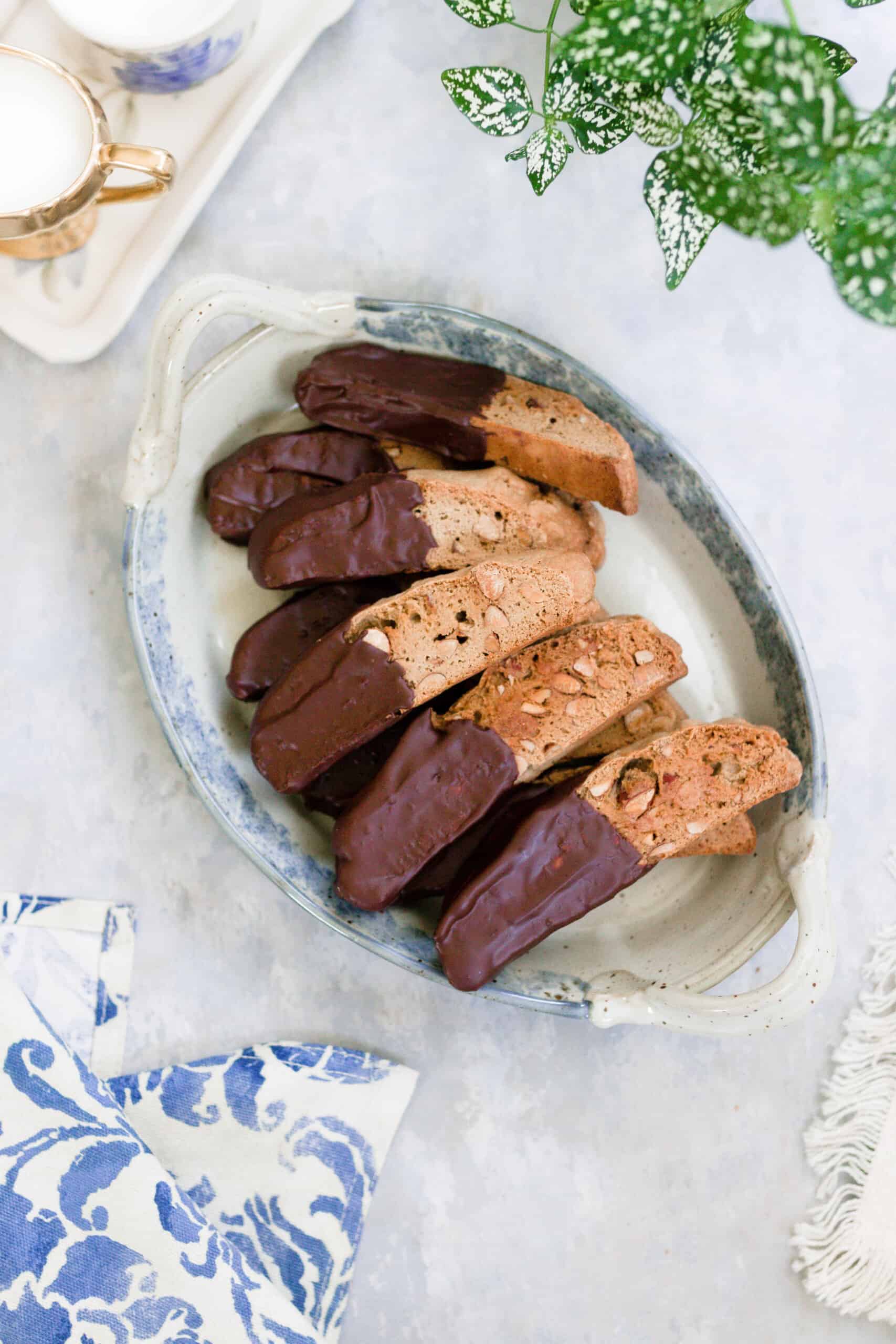 sourdough biscotti dipped in chocolate on a white and blue vintage platter on a gray countertop with a blue floral towel in the right corner