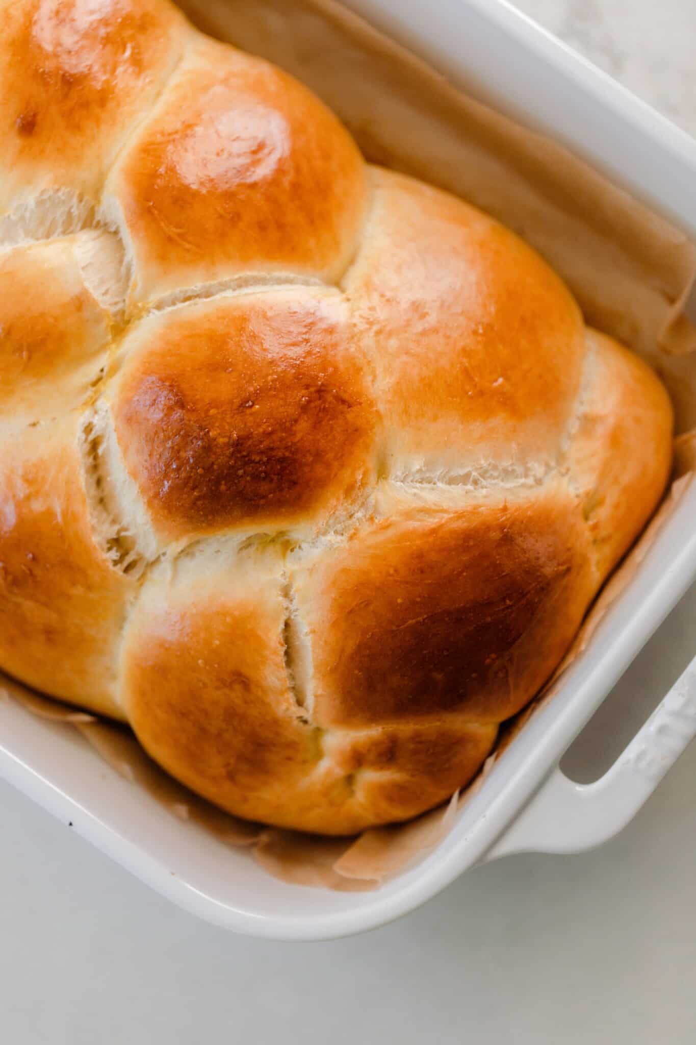 golden braided sourdough challah loaf in a white baking dish in an angle on a white countertop