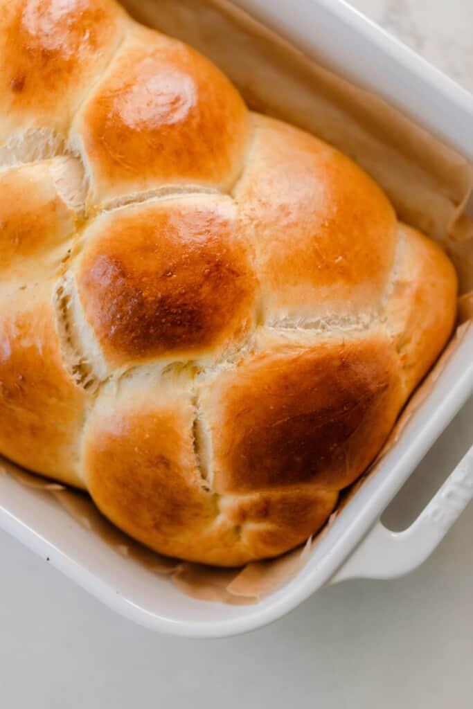 golden braided sourdough challah loaf in a white baking dish in an angle on a white countertop