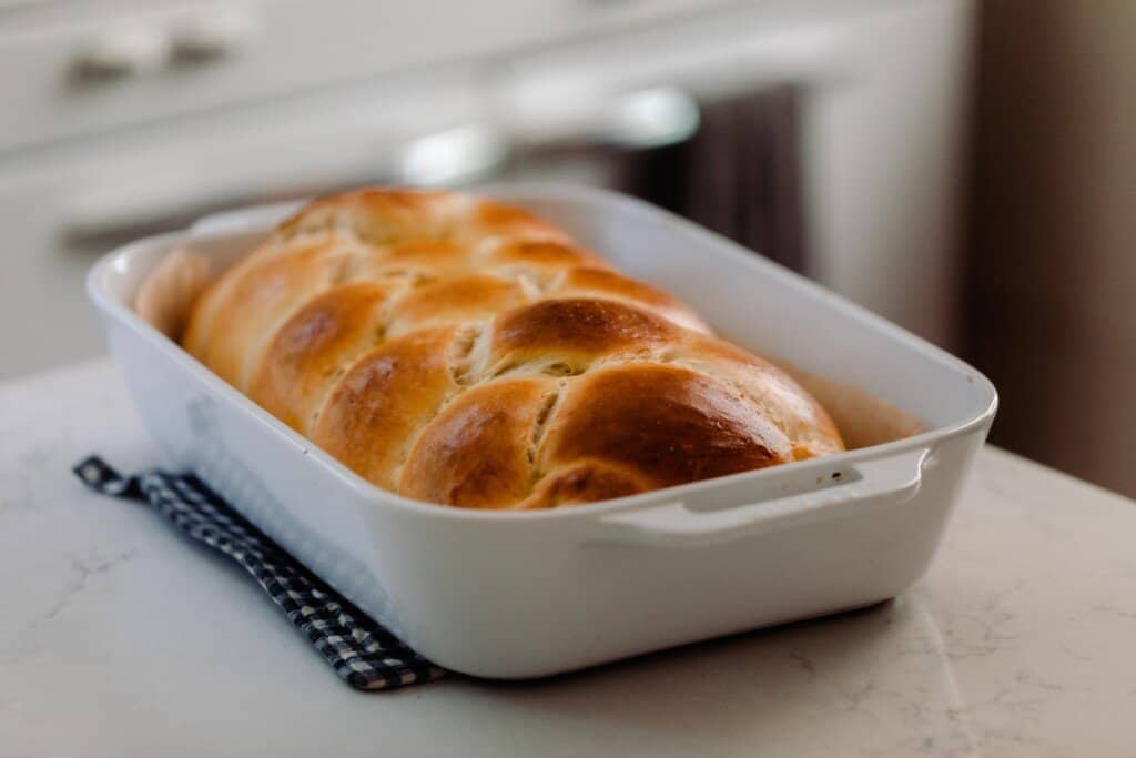sourdough challah fresh out of the opven in a white baking dish on a pot holder on a white countertop
