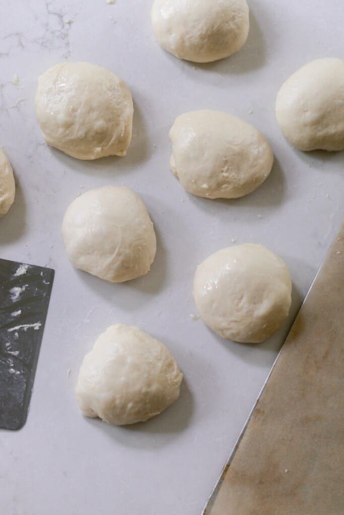 eight balls of dough on a white quartz countertop next to a bench scraper