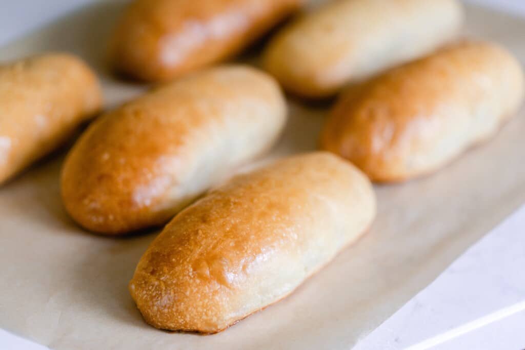 six sourdough hot dog buns with a gorgeous golden brown crust on parchment paper