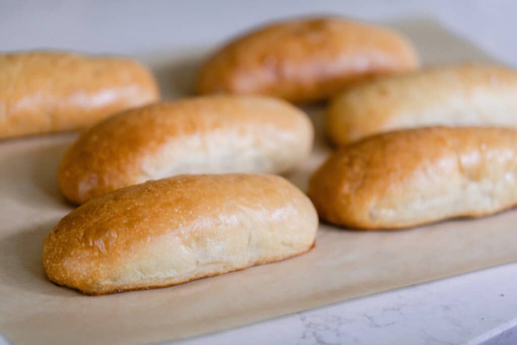 side view of six sourdough hot dot buns on parchment paper