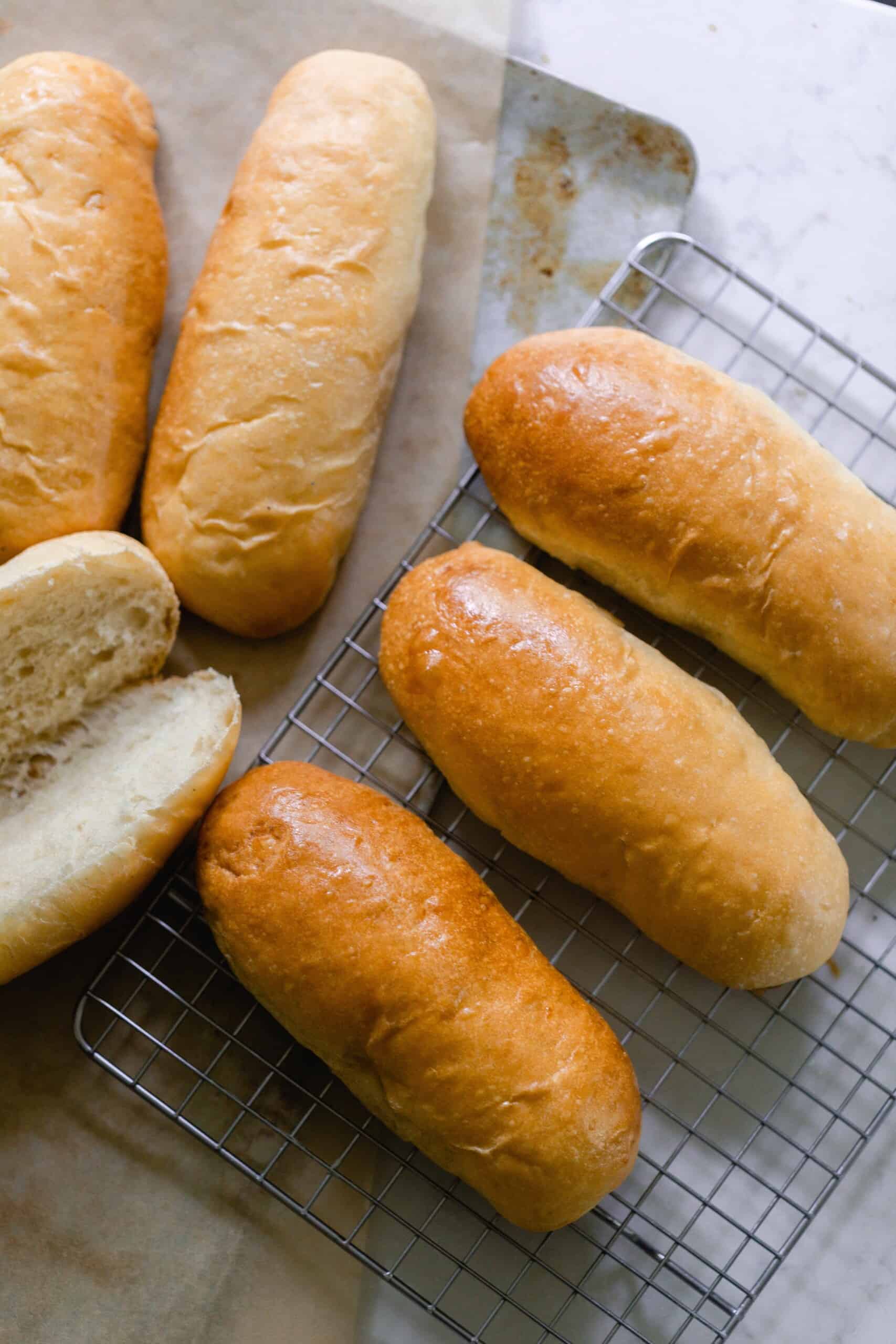 6 sourdough hot dog buns on a wire rack with one sliced open