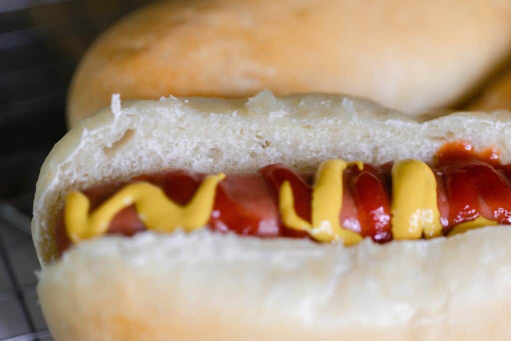 close up of a sourdough hot dog bun cut down the side with a hot dog with ketchup and mustard nestled inside