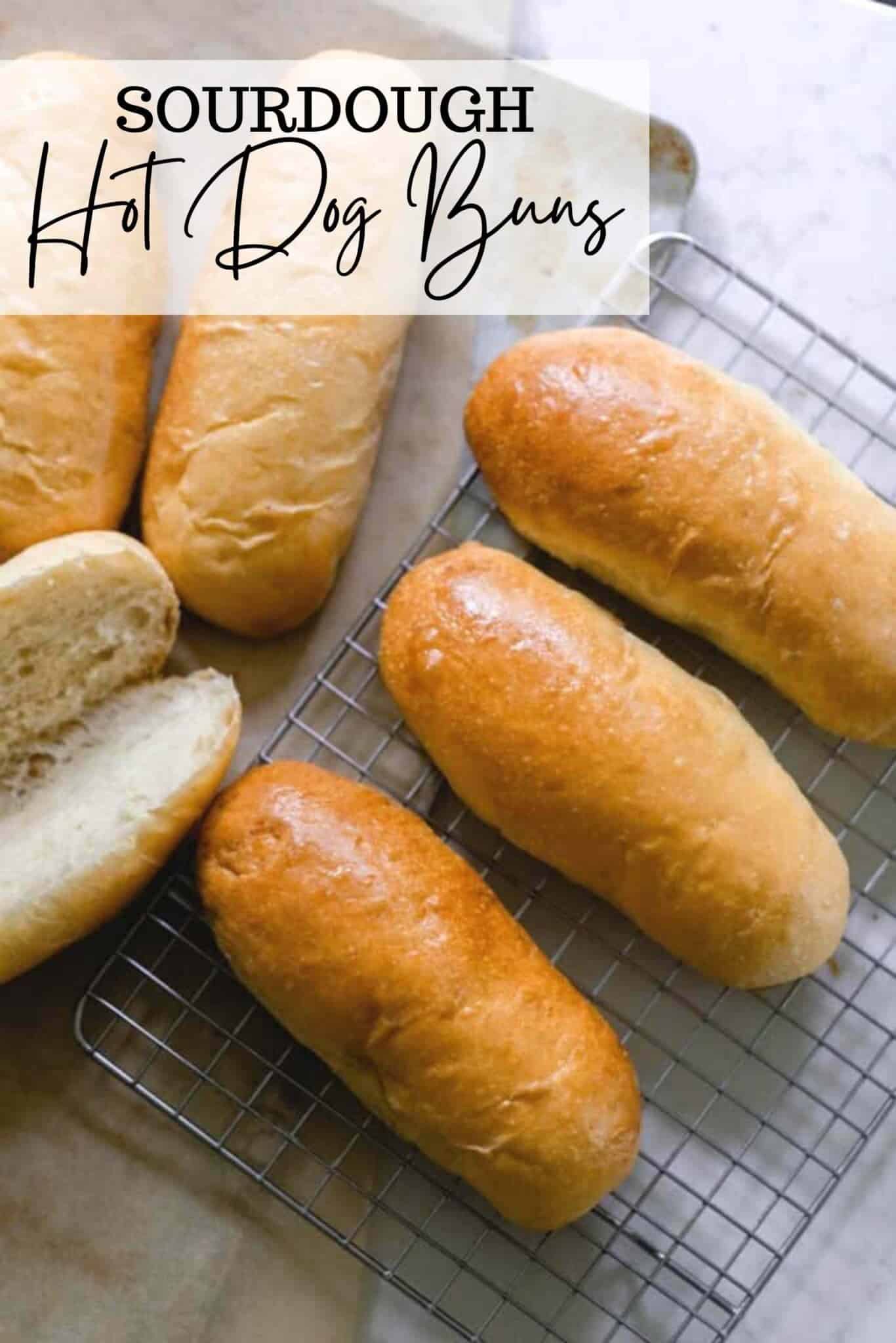 6 sourdough hot dog buns on a wire rack with one sliced open