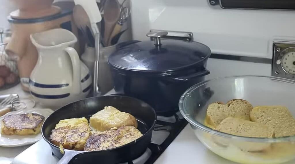 cooking brioche French toast on a cast iron skillet on a antique stove with a bowl of the egg mixture to the right