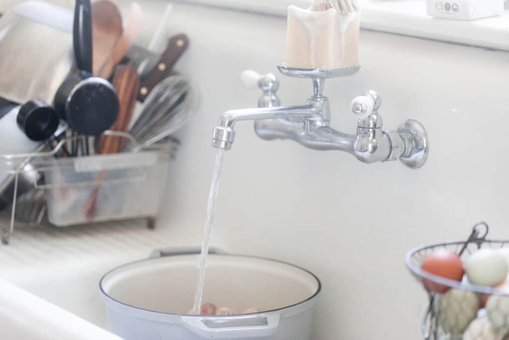 a gray dutch oven in a sink being filled with water