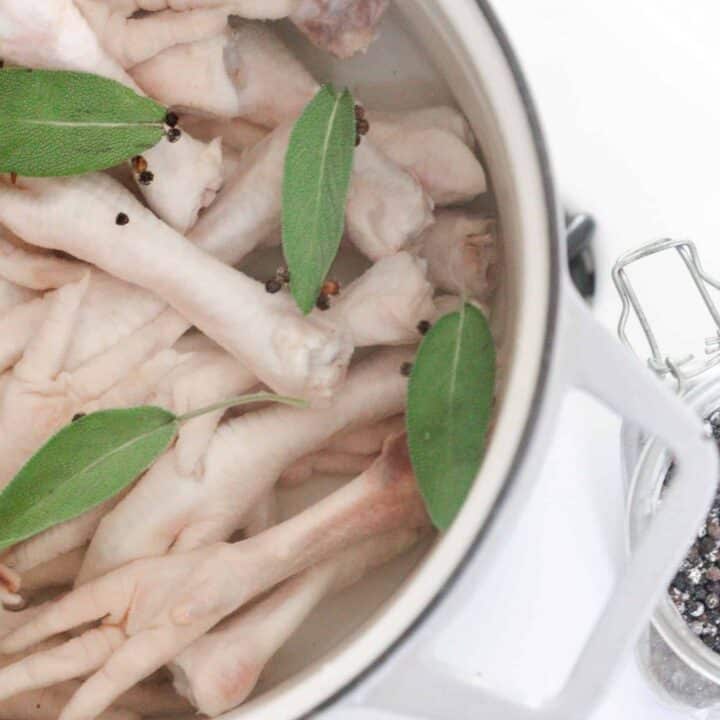 chicken feet with bay leaves and water in a white dutch oven on a stove