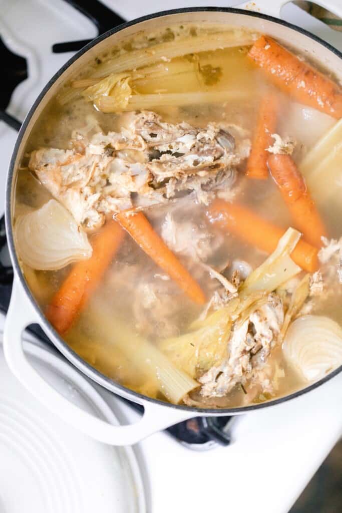 overhead photo of chicken bones, lettuce, celery and carrots in a dutch oven on the stove