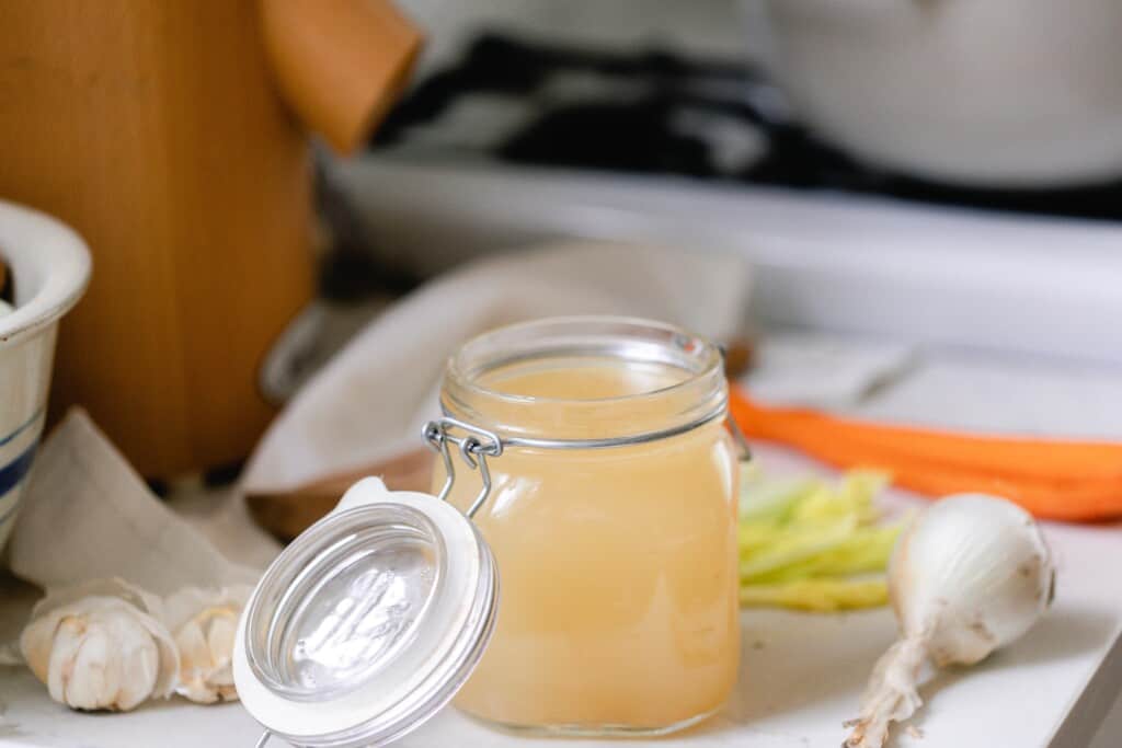 homemade bone broth in a swing top lid on a white countertop surrounded by veggies