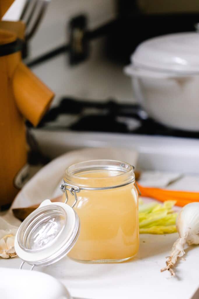 swing top jar of homemade bone broth on a white kitchen countertop with an antique stove in the background