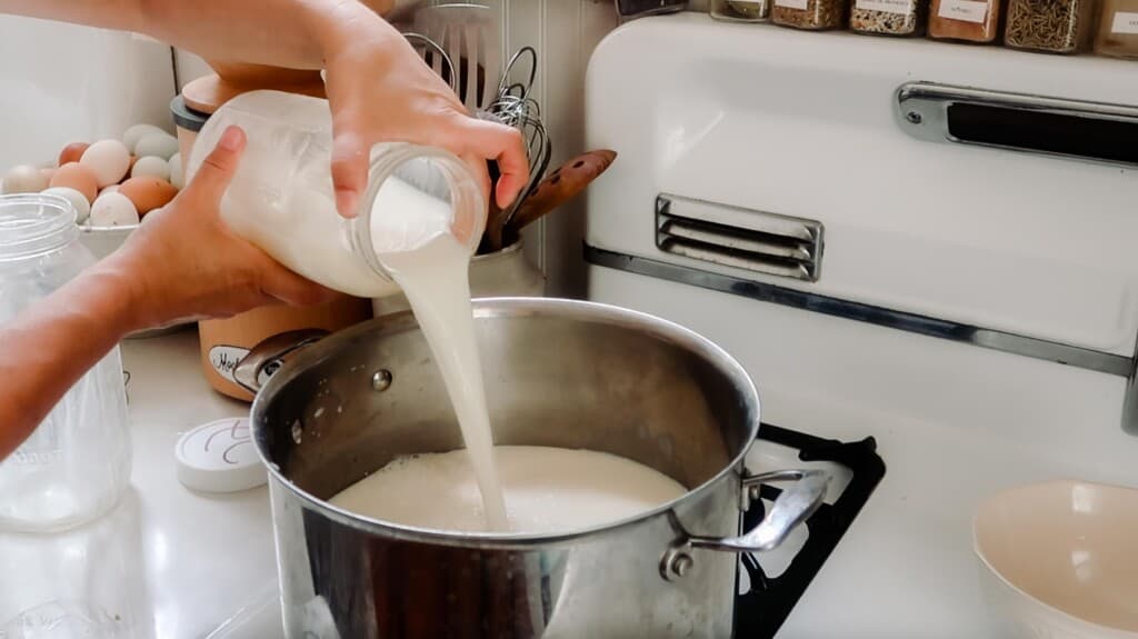 jar of milk being poured into a large stainless pot with citric acid and water