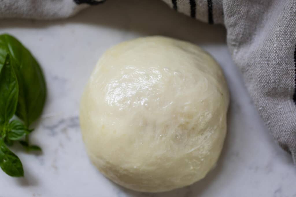 ball of fresh mozzarella cheese on a white countertop with a white towel and basil 