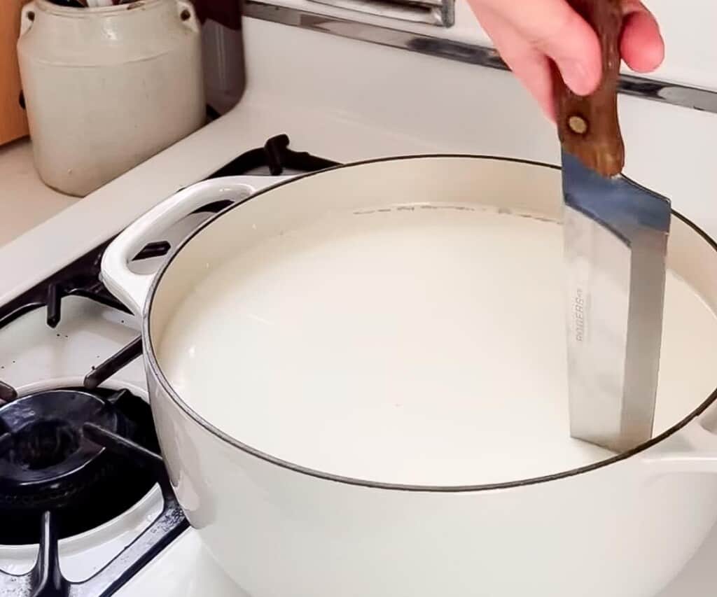 cutting curds with a large knife in a white dutch oven